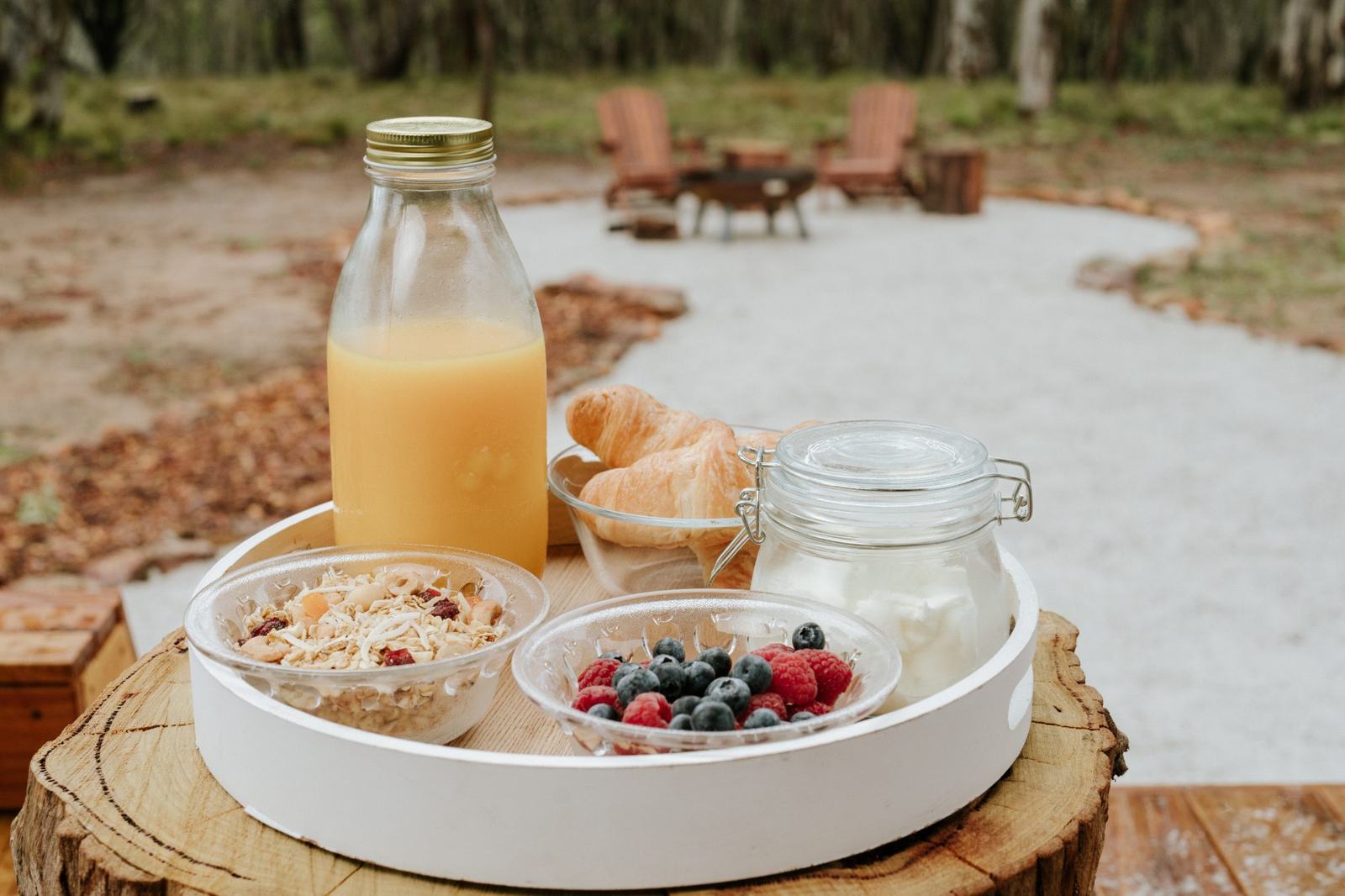 Breakfast tray of juice, granola and fresh berries on a timber stump