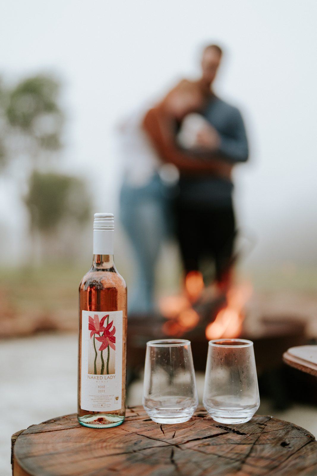 Rosé and glasses on a stump by the fire at dusk