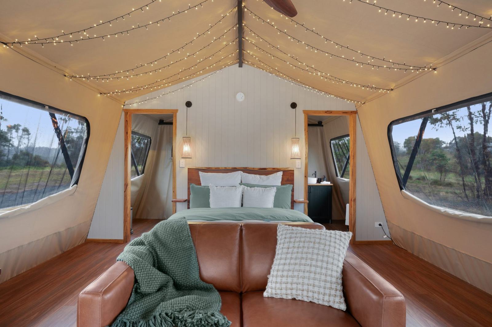Glamping tent interior with warm lighting, queen bed & leather sofa